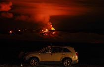 Un hombre habla por teléfono en su coche junto a Saddle Road mientras el volcán Mauna Loa entra en erupción el miércoles 30 de noviembre de 2022, cerca de Hilo, Hawái.