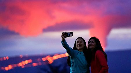 Ingrid Yang, left, and Kelly Bruno, both of San Diego, take a photo in front of lava erupting from Hawaii's Mauna Loa volcano on Wednesday, 30 November.