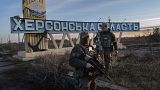 Two Ukrainian defence forces members stand next to a sign reading "Kherson region" in the outskirts of Kherson, 14 November 2022