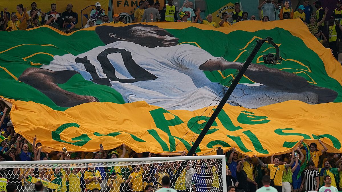 مشجعو كرة القدم يحملون العلم البرازيلي العملاق مع صورة بيليه ورسالة كتب عليها باللغة الإنجليزية: "نرجو لك الشفاء العاجل" في ملعب لوسيل في الدوحة. 2022/11/02