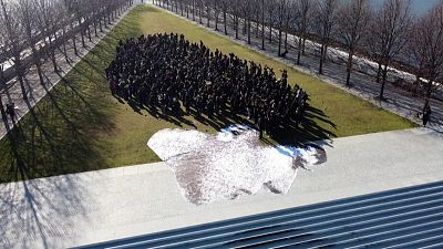 Hundreds gather on New York's Roosevelt Island to join one of French artist JR's participatory performances, standing alongside a portrait of 16-year-old Iranian Nika Shahkara