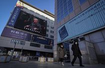 Residents walk by a live broadcast of the memorial service for late Chinese President Jiang Zemin. Tuesday, 6 December 2022.