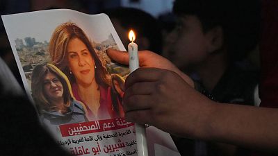 A Palestinian holds a light candle and a picture of slain Al Jazeera journalist Shireen Abu Akleh.