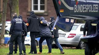 An suspect, second right, is escorted from a police helicopter by police officers after the arrival in Karlsruhe, Germany, Wednesday, Dec. 7, 2022.