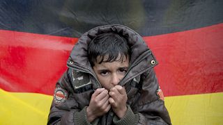 طفل سوري على خلفية علم ألمانيا في محطة الحدود الشمالية اليونانية إيدوميني.