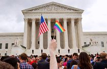 فردی مقابل دادگاه عالی واشنگتن پرچم رنگین‌کمانی و پرچم آمریکا در دست دارند