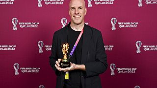 Jornalista Grant Wahl segura numa réplica do troféu do Campeonato do Mundo de Futebol, em Doha, Qatar