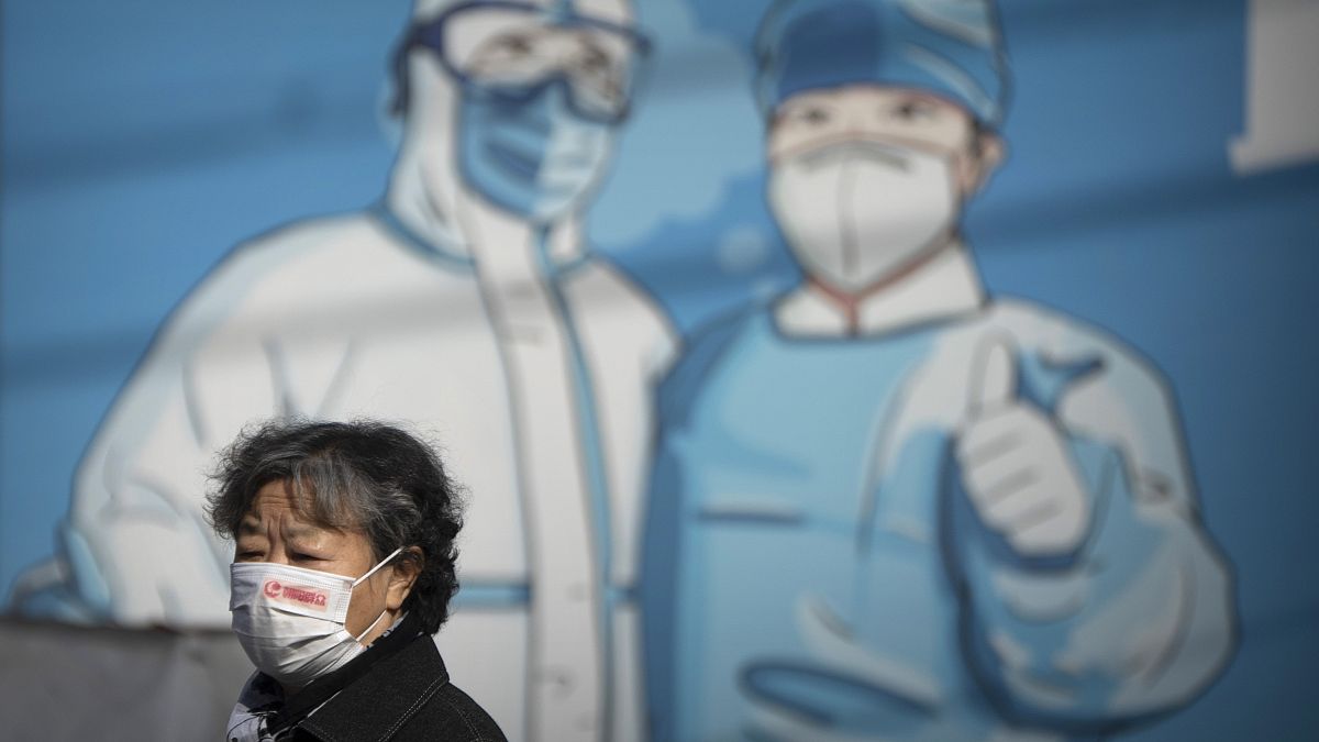 سيدة صينية تمر عبر لوحة جدارية للطاقم الطبي في بكين، الصين.