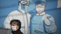 سيدة صينية تمر عبر لوحة جدارية للطاقم الطبي في بكين، الصين.