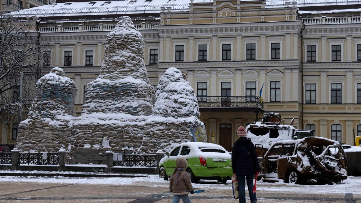 A woman and a child pass by a monument to Princess Olga, covered with sand bags to protect it from shelling, near damaged Russian military vehicles in Kyiv, Dec. 12, 2022.