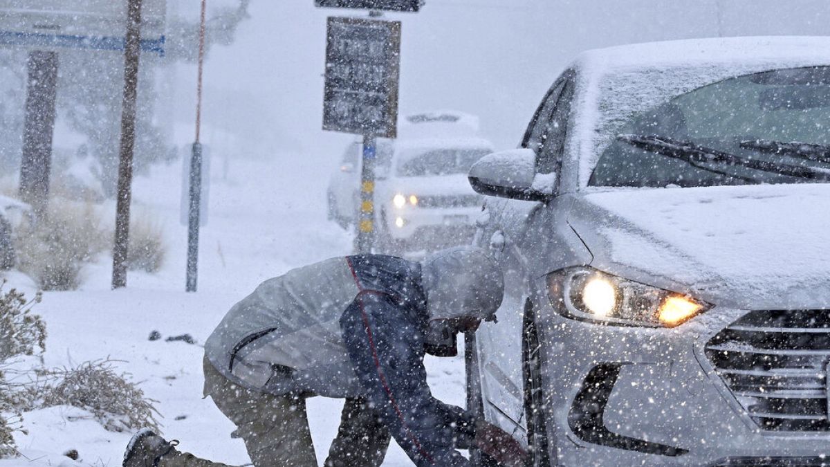 Evan Freedman, de Los Ángeles, pone cadenas de nieve en su vehículo mientras cae una intensa nevada en la autopista 2 cerca de Wrightwood, California.