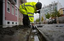 A municipal worker clears the drains in a street that was flooded during heavy rain overnight in Alges, just outside Lisbon, Tuesday, Dec. 13, 2022.