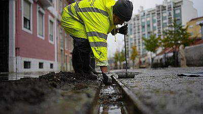 A municipal worker clears the drains in a street that was flooded during heavy rain overnight in Alges, just outside Lisbon, Tuesday, Dec. 13, 2022.
