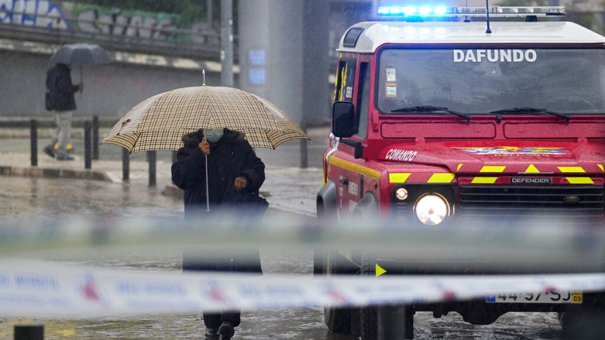People walk under the rain next to a firefighters' command vehicle where some streets were flooded in Alges, just outside Lisbon.