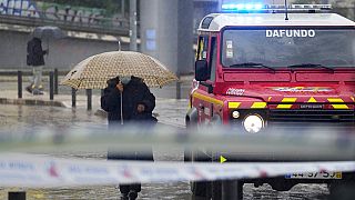 People walk under the rain next to a firefighters' command vehicle where some streets were flooded in Alges, just outside Lisbon.