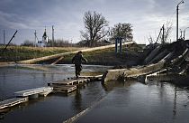 Idoso atravessa curso de água sobre ponte improvisada, na Ucrânia