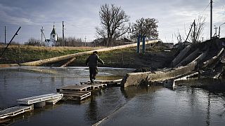 Idoso atravessa curso de água sobre ponte improvisada, na Ucrânia