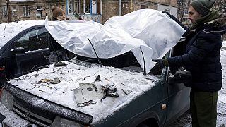 Una pareja cubre su coche dañado con una lona de plástico tras un ataque ruso en Kiev, Ucrania, el miércoles 14 de diciembre de 2022.