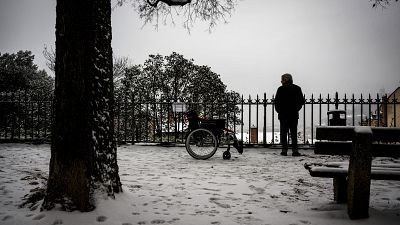 فرنسي يقف بجانب كرسي متحرك في شارع مغطى بالثلج في ليون، جنوب شرق فرنسا