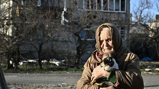 Local resident Galyna, 80, holds a cat in front of a damaged building where she lives without electricity, water and heat, in the town of Lyman, Donetsk region