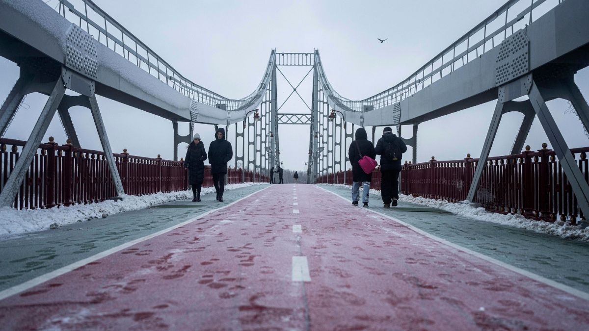 People walk on pedestrian bridge across the Dnipro river in Kyiv, Ukraine, Thursday, Dec. 15, 2022.
