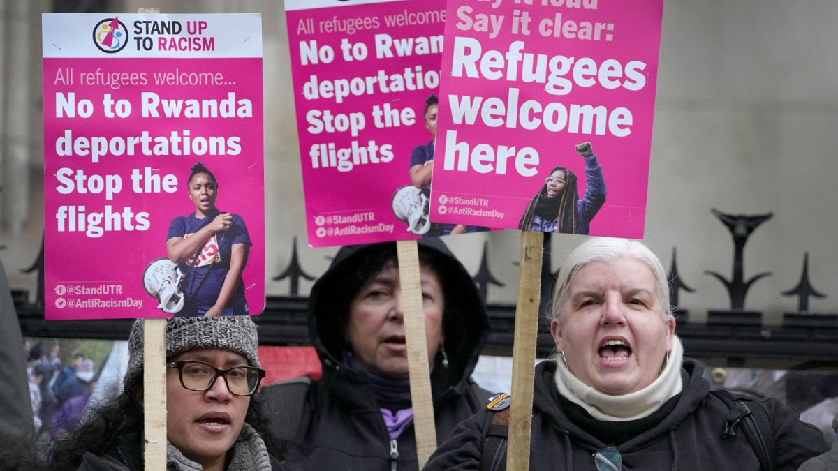 Stand Up To Racism campaigners hold banners outside the High Court in London, Monday, Dec. 19, 2022.
