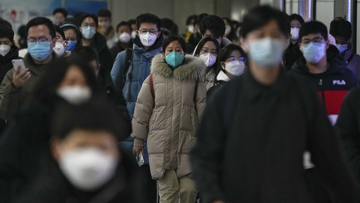 Masked commuters walk through a walkway in between two subway stations as they head to work during the morning rush hour in Beijing, 20 December 2022