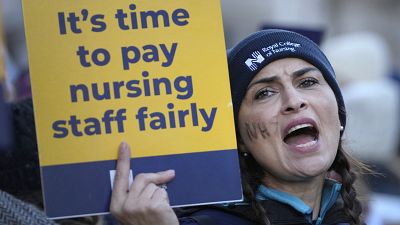 ممرضة ترفع لافتة كتب عليها "حان الوقت لدفع رواتب طواقم التمريض بإنصاف"