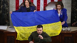 La vicepresidenta Kamala Harris y la presidenta de la Cámara de Representantes, Nancy Pelosi, sujetan una bandera ucraniana firmada por las tropas en Bajmut