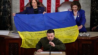VP Kamala Harris and House Speaker Nancy Pelosi react as Ukrainian President Volodymyr Zelenskyy presents lawmakers with a Ukrainian flag autographed by soldiers in Bakhmut