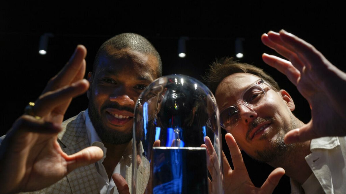Calvin Jong-A-Pin, sales and marketing specialist at Gassan Diamonds, left, and artist Pablo Lücker, right, pose with the smallest work of art on a diamond, an engraved heart.