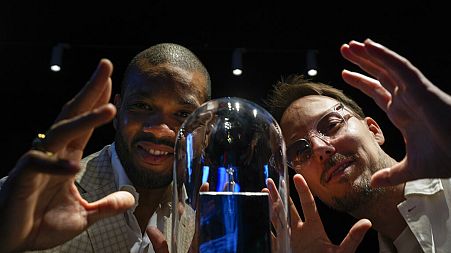 Calvin Jong-A-Pin, sales and marketing specialist at Gassan Diamonds, left, and artist Pablo Lücker, right, pose with the smallest work of art on a diamond, an engraved heart.