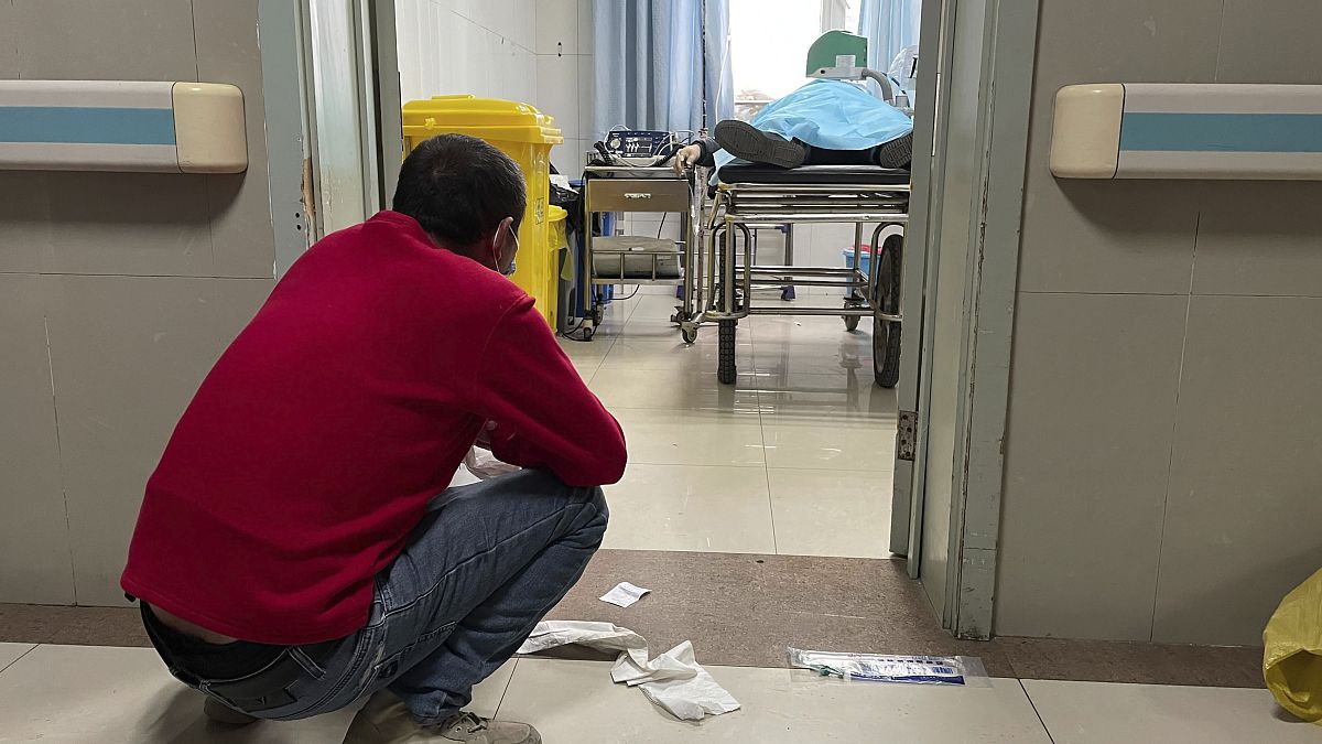 رجل يجلس القرفصاء خارج غرفة العلاج، حيث يتلقى شخص مسن مصاب بـ"كوفيد" المساعدة في التنفس عبر مضخة تهوية في قسم الطوارئ بمستشفى باودينغ بمدينة تشوتشو، شمال الصين، 21 ديسمبر 2022