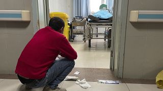 رجل يجلس القرفصاء خارج غرفة العلاج، حيث يتلقى شخص مسن مصاب بـ"كوفيد" المساعدة في التنفس عبر مضخة تهوية في قسم الطوارئ بمستشفى باودينغ بمدينة تشوتشو، شمال الصين، 21 ديسمبر 2022
