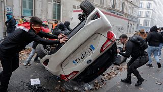 Manifestantes vuelcan un coche durante una protesta contra el reciente tiroteo en el centro cultural kurdo de París, el 24 de diciembre de 2022.