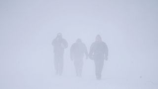 ثلاثة أشخاص يسيرون وسط الثلوج الكثيفة التي غطت بافالو في نيويورك