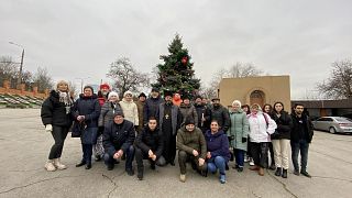 Μέλη της ελληνικής κοινότητας στη Ζαπορίζια στο προαύλιό της Αρμενικής Εκκλησίας με φόντο το χριστουγεννιάτικο δέντρο