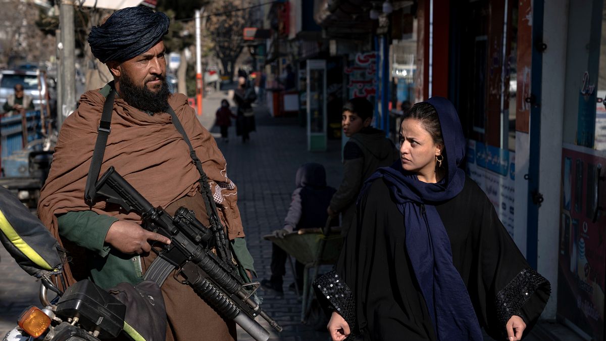 A Taliban fighter stands guard as a woman walks past in Kabul, Afghanistan