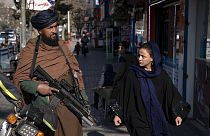 Mulher passa ao lado de um talibã armado, no Afeganistão