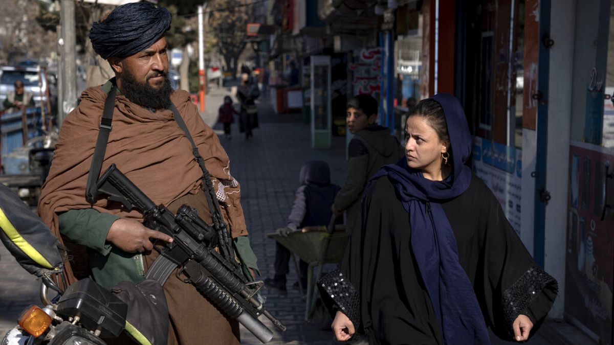 Une femme afghane marche dans la rue à côté d'un taliban (26.12.22).
