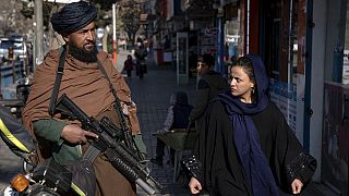 Une femme afghane marche dans la rue à côté d'un taliban (26.12.22).