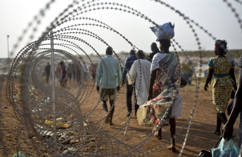 displaced people walk next to a razor wire fence at the United Nations base in the capital Juba, South Sudan, January 2016