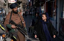Un combattant taliban monte la garde alors qu'une femme lui passe devant à Kaboul, en Afghanistan, le 26 décembre 2022.