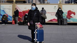 مسافرة تنتظر خارج محطة سكة حديد بكين مع حقيبتها في بكين، الصين 2022.