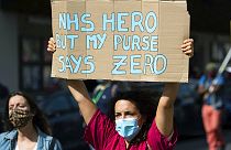 Tüntető tart magasra egy táblát a 2020 szeptemberében tartott, az NHS dolgozóinak követelt béremelések miatti demonstrációk egyikén