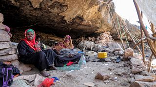 نساء وأطفال في اليمن يجلسون على الأرض في كوخ بجوار كهف حيث لجأت عائلة إلى مأوى بسبب الفقر ونقص السكن.