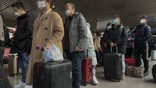 People in China wearing face masks with their luggage as they prepare to travel.