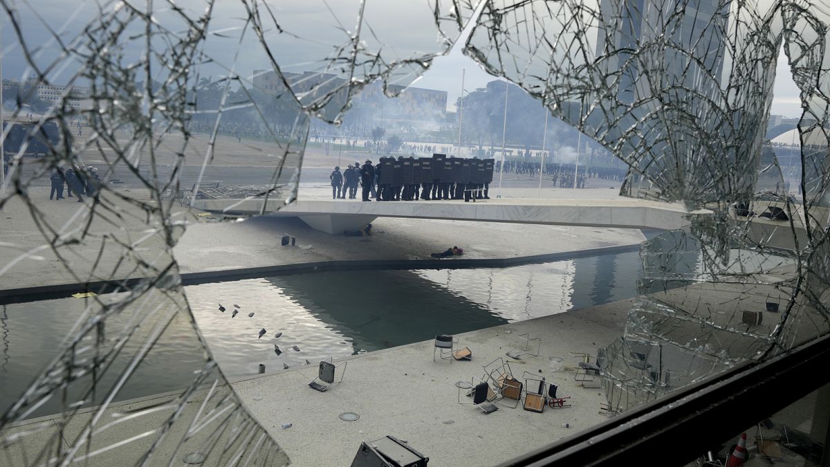 Police stand on the other side of a window at Planalto Palace that was shattered by protesters. Sunday, 8 January 2023.