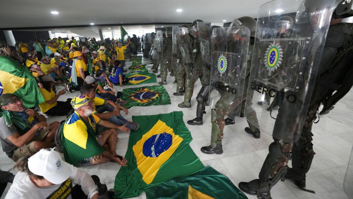  المتظاهرون، أنصار الرئيس البرازيلي السابق جايير بولسونارو، يجلسون أمام الشرطة داخل قصر بلانالتو بعد اقتحامه، في برازيليا، البرازيل،  8 يناير 2023