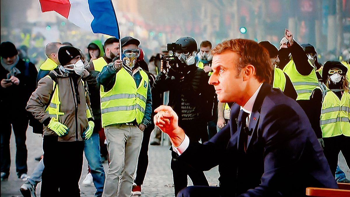 الرئيس الفرنسي إيمانويل ماكرون أمام صورة لاحتجاجات السترات الصفراء. 